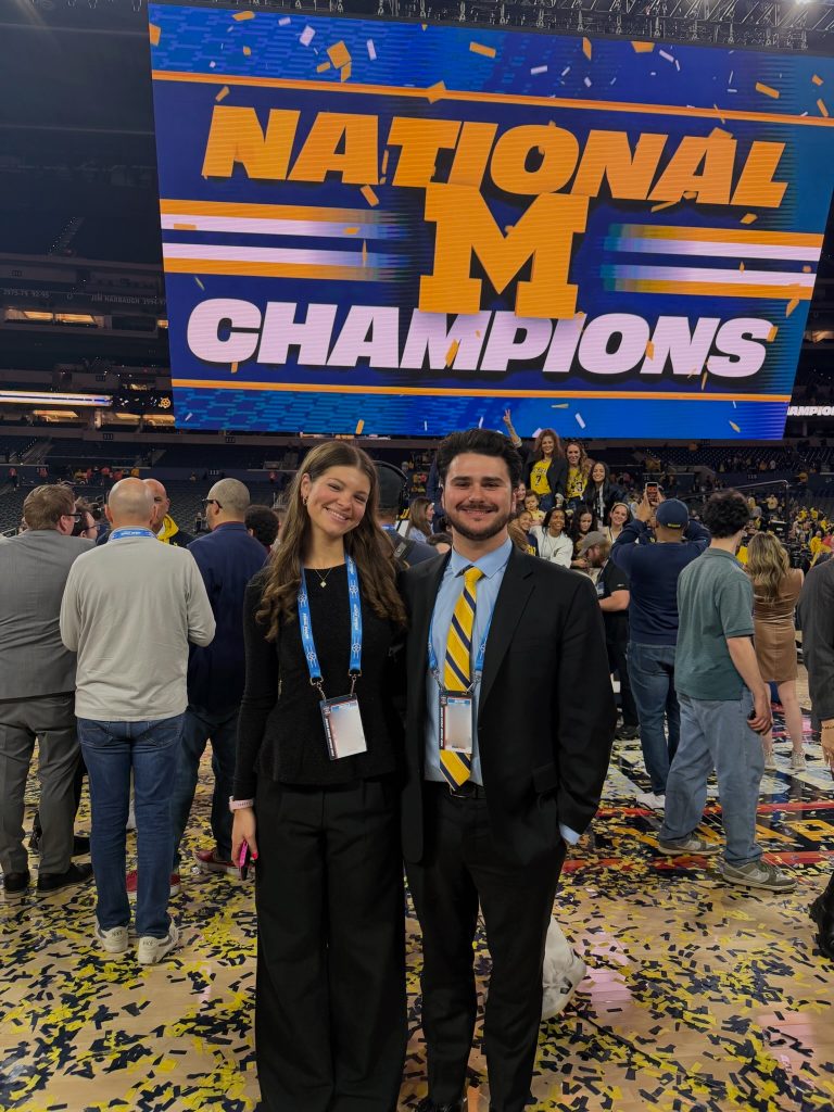 Two WCBN Sports broadcasters standing on the court covered in yellow and blue confetti.